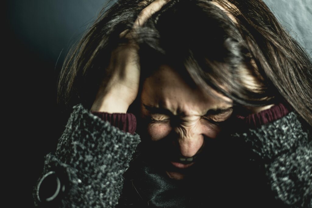 Close-up of a woman in distress with eyes closed and hands in hair, expressing anxiety.